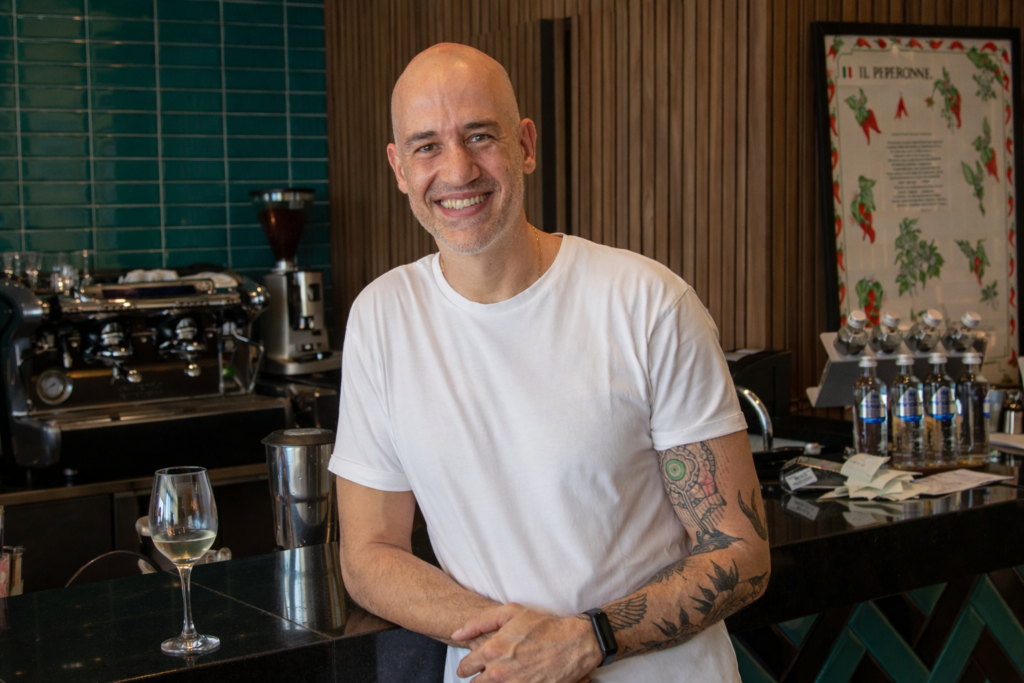 Marcelo Reis, proprietário do La Pasta Gialla em Salvador, sorri apoiado no balcão do restaurante.