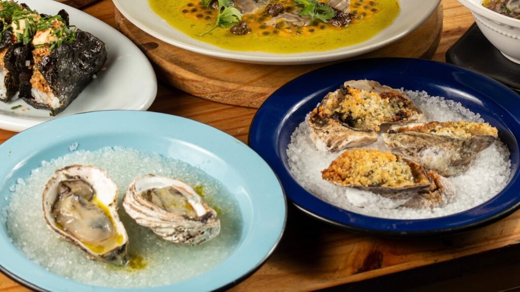 Variedade de pratos com ostras frescas e empanadas em pratos coloridos. Foto: Guiga Mota