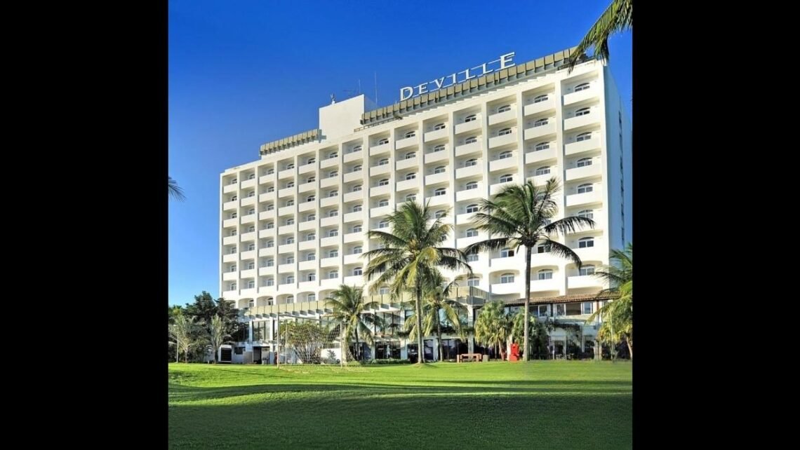 O Deville Prime Salvador exibe sua fachada com o nome do hotel visível, cercado por área verde e coqueiros.