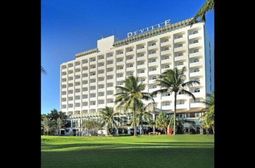 O Deville Prime Salvador exibe sua fachada com o nome do hotel visível, cercado por área verde e coqueiros.