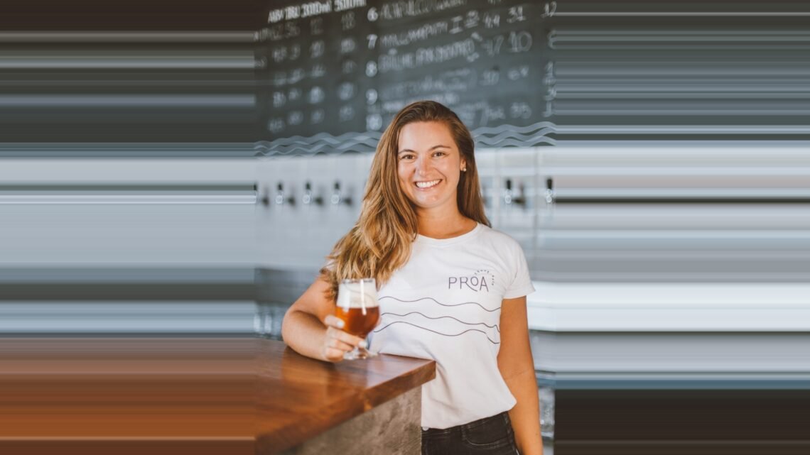Débora Lehnen sorrindo com uma taça de cerveja na mão, representando a liderança da Proa Cervejaria.