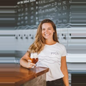 Débora Lehnen sorrindo com uma taça de cerveja na mão, representando a liderança da Proa Cervejaria.