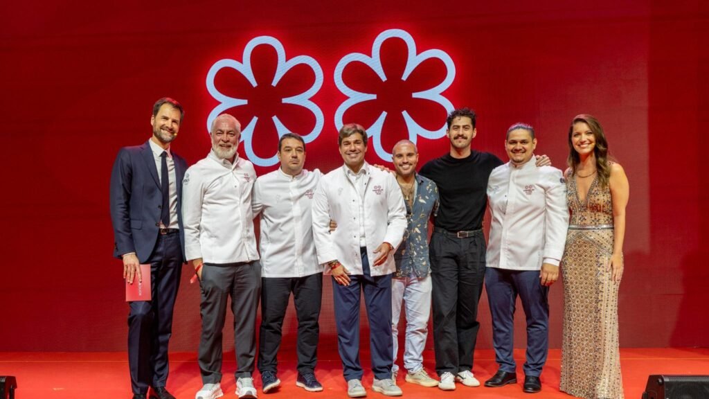 Chefs premiados durante cerimônia do Guia Michelin Brasil 2026 no palco com símbolo das estrelas ao fundo