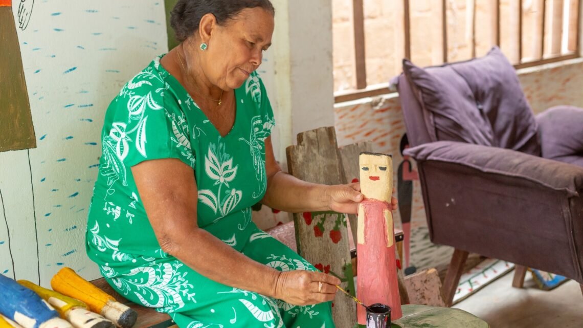 Vanusa pinta escultura em madeira à mão em Alagoas, técnica tradicional do artesanato local.