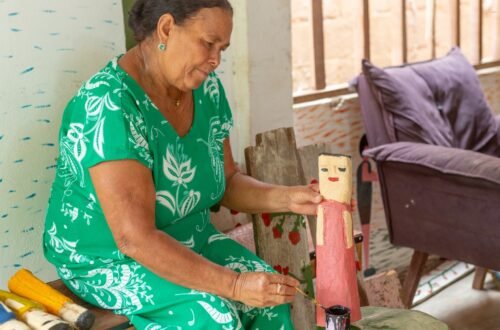 Vanusa pinta escultura em madeira à mão em Alagoas, técnica tradicional do artesanato local.