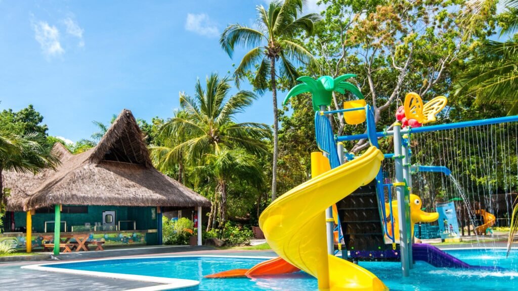 Parque aquático infantil colorido com escorregadores e chuveiro em formato de coqueiro no Tivoli Ecoresort Praia do Forte, cercado por vegetação.