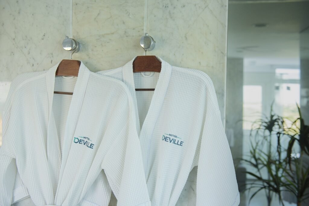 Dois roupões brancos do Deville Prime Salvador pendurados em cabides no banheiro de um apartamento do hotel.