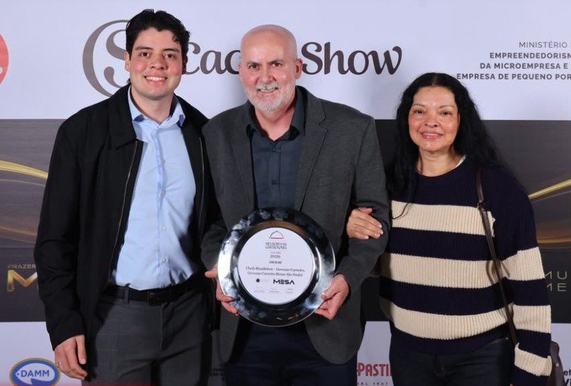 Giovanni Guimarães recebe o prêmio de Livro do Ano no Melhores da Gastronomia 2026 ao lado de familiares, em São Paulo.