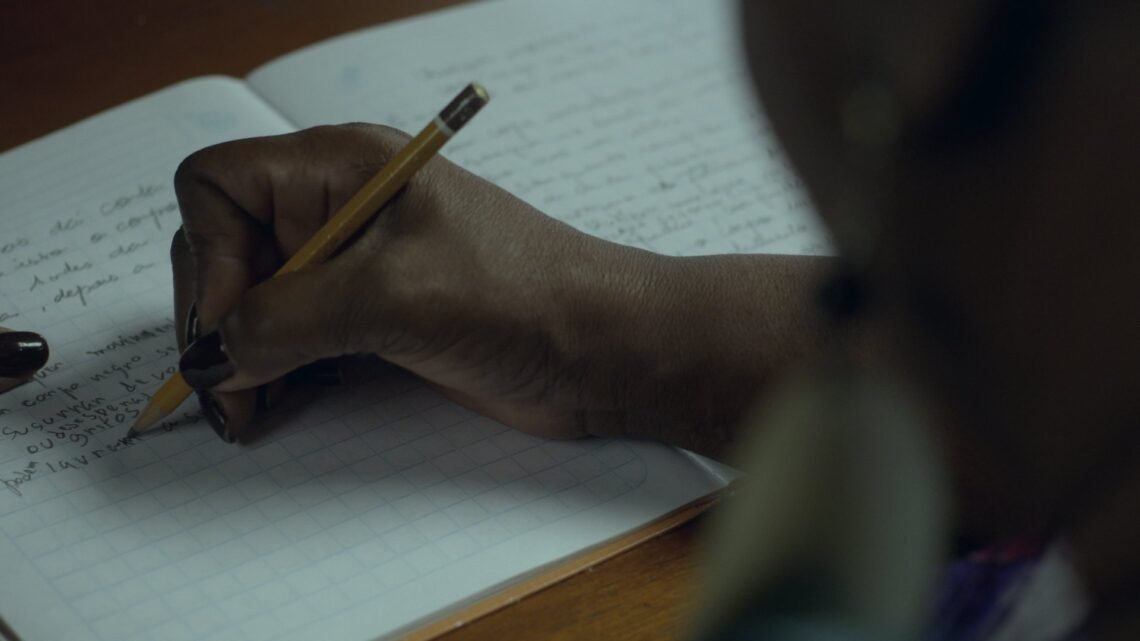 Pessoa escreve em um caderno em cena da série Elas no Singular, que retrata a trajetória de oito escritoras brasileiras e seus processos de criação literária.