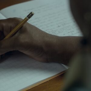 Pessoa escreve em um caderno em cena da série Elas no Singular, que retrata a trajetória de oito escritoras brasileiras e seus processos de criação literária.