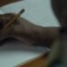 Pessoa escreve em um caderno em cena da série Elas no Singular, que retrata a trajetória de oito escritoras brasileiras e seus processos de criação literária.