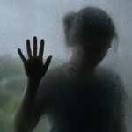 Silhueta de uma mulher atrás de um vidro molhado representa a violência doméstica no contexto dos 20 anos da Lei Maria da Penha.