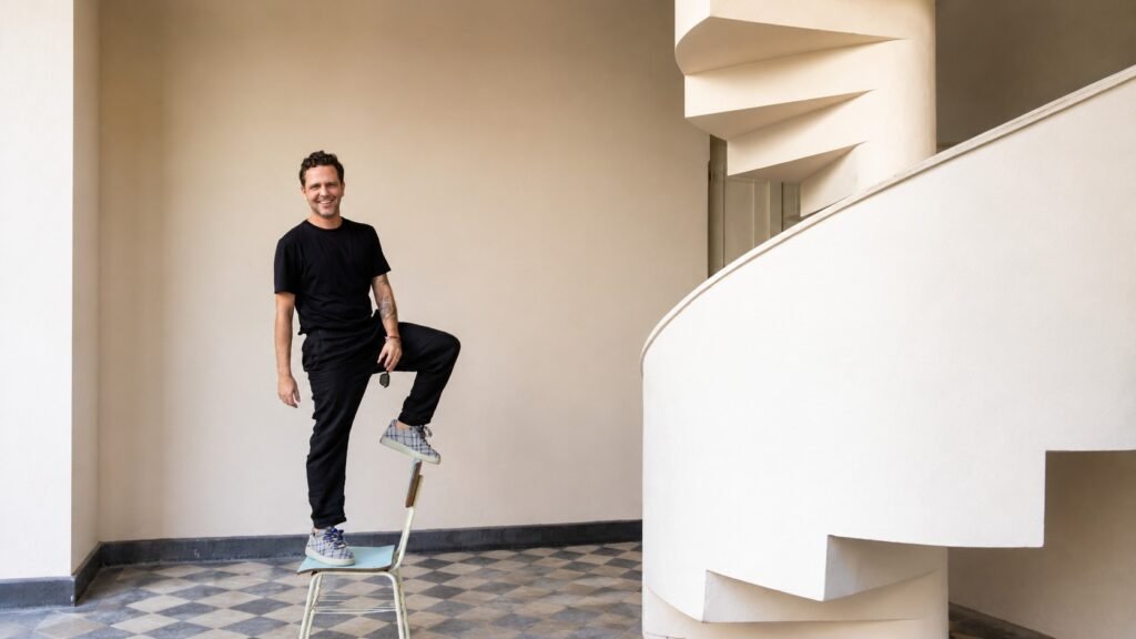 Arquiteto Rodrigo Cassieri em ambiente de arquitetura com escada curva ao fundo.