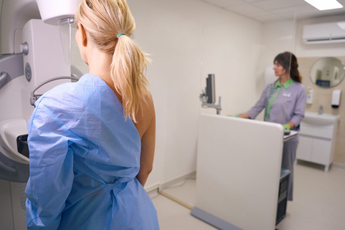 Paciente se prepara para exame de mamografia digital pelos planos de saúde, acompanhada por profissional em clínica.