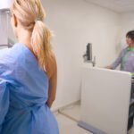 Paciente se prepara para exame de mamografia digital pelos planos de saúde, acompanhada por profissional em clínica.