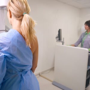Paciente se prepara para exame de mamografia digital pelos planos de saúde, acompanhada por profissional em clínica.