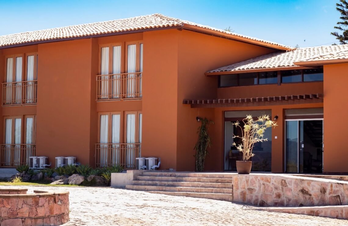 Fachada do Casarão Alpina, em Mucugê, com paredes em tom terracota, varandas e entrada com degraus.