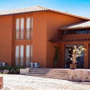 Fachada do Casarão Alpina, em Mucugê, com paredes em tom terracota, varandas e entrada com degraus.