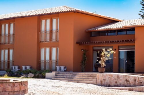 Fachada do Casarão Alpina, em Mucugê, com paredes em tom terracota, varandas e entrada com degraus.