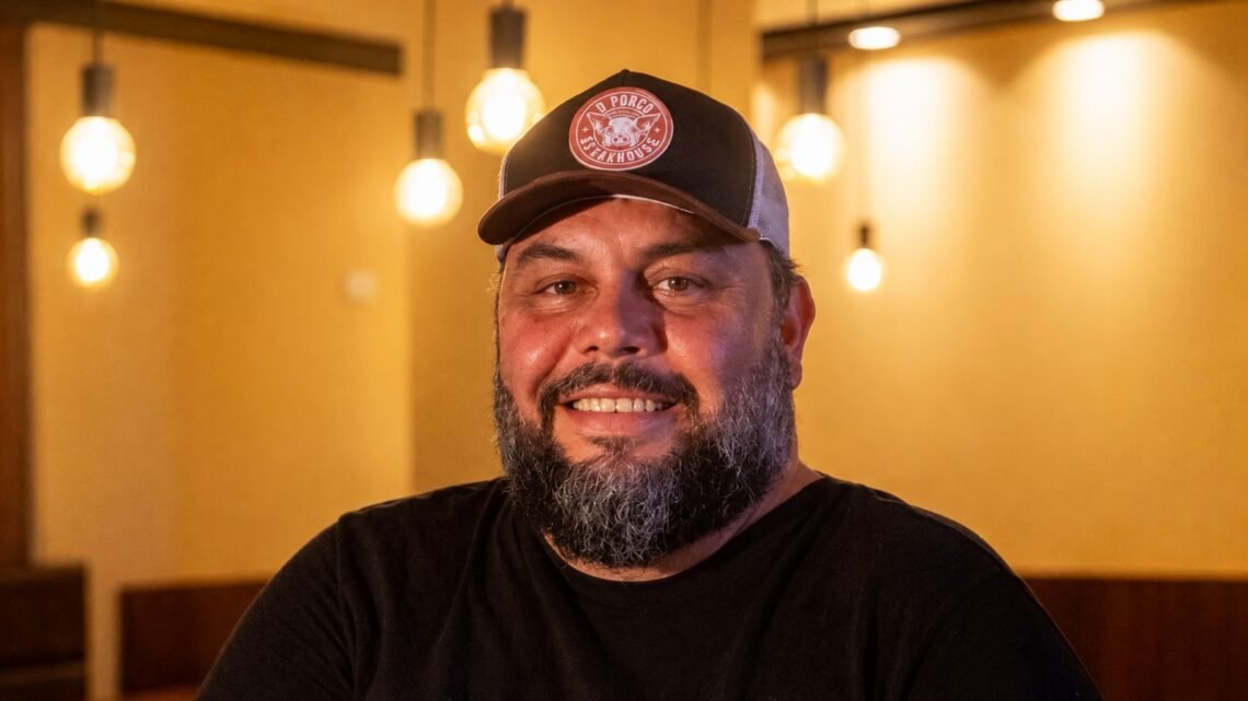 Sandro Borges, chef convidado do PorcoDay Reconvexo, com boné e camiseta preta em ambiente de restaurante.