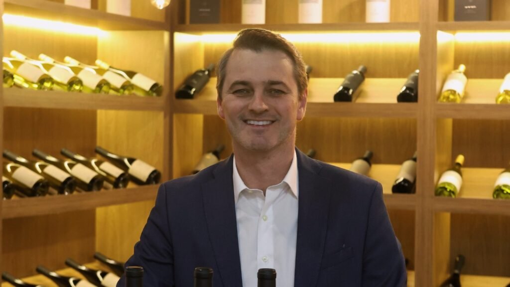 Fabiano Borré, CEO da UVVA, atrás de uma mesa com garrafas de vinho.