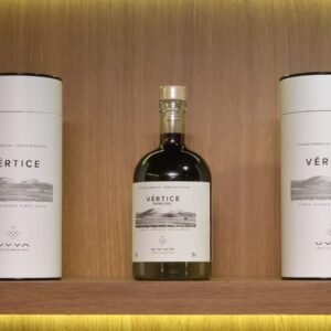 Garrafa do Vértice, primeiro vinho licoroso da UVVA, entre duas embalagens em uma prateleira de madeira.